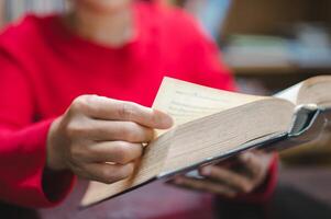 Person in vibrant red sweater holds an open book, delicately turning page, embodying joy of reading and learning in warm, inviting environment photo