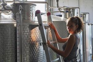 a female winemaker checking the quality of the wine on a ladder above the cistern photo