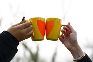 close-up of a toast between two yellow cups with a red heart printed on them held aloft by two female hands with well-manicured nails photo