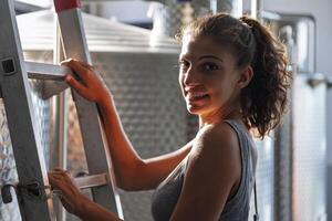 a female winemaker checking the quality of the wine on a ladder above the cistern photo