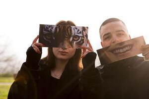 portrait of two young lovers having fun showing a fantasy pictures partially covering their faces in a public park in winter photo