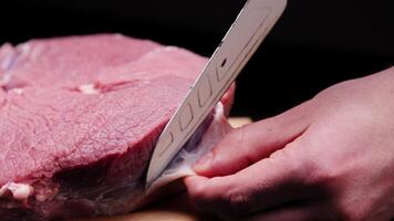 A butcher removes the fascia from a beef steak with a large knife in a dark room video