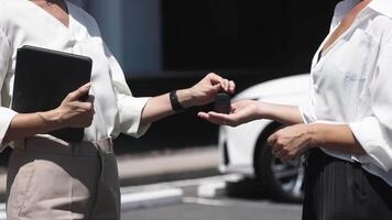 Faceless auto dealer giving key of new white car to crop male client in salon, outdoor. Businessman exchange handing over the car keys for to a young woman. New purchase in a showroom video