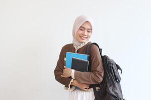 Smiling Muslim Student Girl Holding Books and Backpack Against White Wall photo