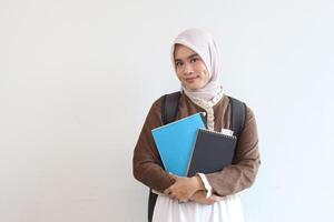 Smiling Muslim Student Girl Holding Books and Backpack Against White Background photo