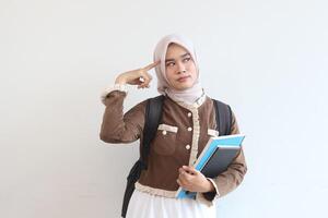 Thoughtful Muslim Student Girl Holding Books and Backpack Against White Background photo