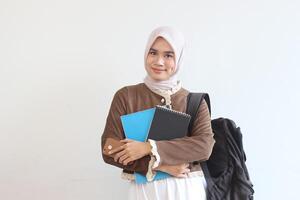 Portrait of a Smiling Muslim Student Holding Books and Backpack Against White Background photo