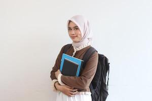Portrait of a Smiling Muslim Female Student Holding Books and Backpack Against White Background photo