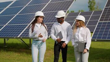 Group of three multiracial engineers walking at solar station checking solar panels video