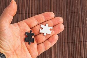 A hand holding two puzzle pieces one white and one black, difficult choice photo