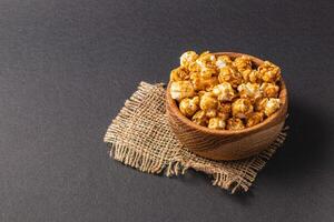 Sweet caramelized popcorn in a wooden bowl on a black background photo