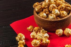 Snack, movie concept, caramelized popcorn in a wooden bowl on a red napkin photo