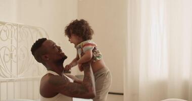 Joyful young ethnic man hugging and playing with adorable toddler video