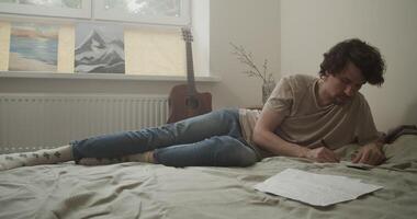 Skilled male songwriter taking notes in notepad while lying on bed video