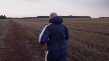 Unrecognizable sportsman running across field with dry grass in evening video
