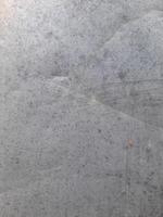 a close-up view of a textured surface a metal sheet, with a dull grayish tone. The surface features a mix of light and dark patches, creating a mottled, weathered, or oxidized appearance photo