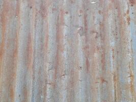 a close-up view of a textured surface a metal sheet, with a dull grayish tone. The surface features a mix of light and dark patches, creating a mottled, weathered, or oxidized appearance photo