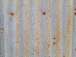 a close-up view of a textured surface a metal sheet, with a dull grayish tone. The surface features a mix of light and dark patches, creating a mottled, weathered, or oxidized appearance photo