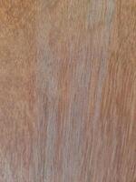 a wooden surface featuring a natural wood grain pattern. The wood has a medium-brown tone with visible horizontal lines, small nail marks, and subtle texture, giving it a raw and organic appearance. photo