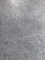 a close-up view of a textured surface a metal sheet, with a dull grayish tone. The surface features a mix of light and dark patches, creating a mottled, weathered, or oxidized appearance photo