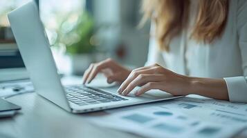 A close-up of hands typing on a laptop while reviewing financial reports on paper documents in an office setting that emphasizes productivity and focus on business growth strategies photo