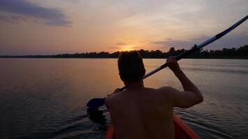 A man kayaks on a calm river towards the sunset. He skillfully rowing oar. Beautiful nature of the evening river. Super Slow Motion video