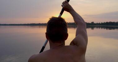 A man kayaks on a calm river towards the sunset. He skillfully rowing oar. Beautiful nature of the evening river. Slow Motion Ultra 4K 50 fps video