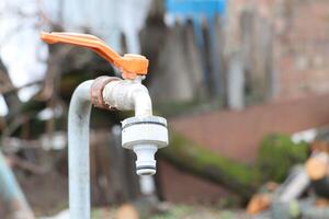 An Outdoor Water Faucet Featuring an Orange Handle Set Against a Rustic Natural Setting photo