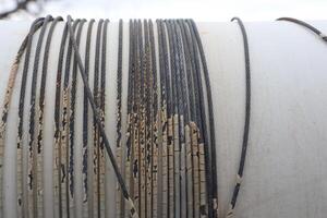 A detailed closeup photo showcasing wornout cables and wires attached to a pipe surface