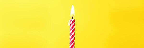 Bright red and white striped birthday candle burning against a vibrant yellow background at a festive celebration photo