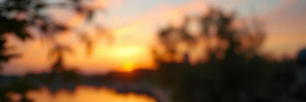 Sun setting over tranquil waters with blurred trees in the foreground creating a serene evening atmosphere photo