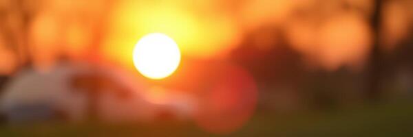 Sunset casting warm hues over a serene landscape with silhouettes of trees and a distant vehicle photo