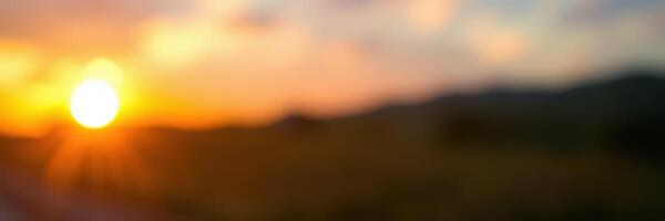 Golden sunset casting a warm glow over the horizon with blurred landscape in the foreground photo