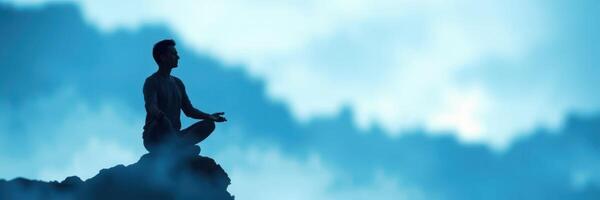 Person practicing meditation on a mountain during a serene day with blue skies and soft clouds photo