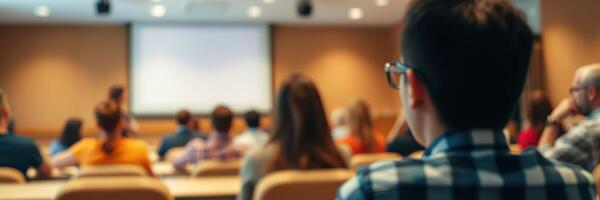 Students engaged in lecture at a conference center while a presenter shares information on a large screen photo