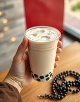 Delicious bubble tea served in a clear cup with ice and tapioca pearls on a wooden table near a window photo