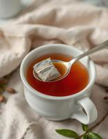 Warm herbal tea steeping in a white cup with a tea bag resting on a spoon over soft fabric backdrop photo