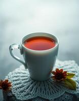 Warm herbal tea in a white cup rests on a knitted coaster decorated with flowers photo