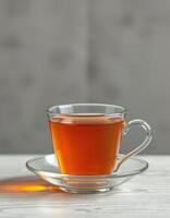 Clear glass cup filled with hot tea on a white wooden table in a softly lit environment photo