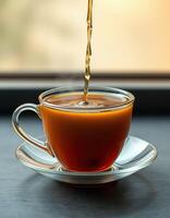 Enjoying a warm cup of tea poured into a glass vessel near a window during a peaceful afternoon moment photo