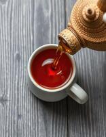 Brewed tea pours into a white cup on rustic wood surface in a cozy setting photo