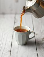 Freshly brewed tea is poured into a classic white cup on a rustic wooden table in the morning light photo