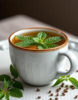 Fresh mint tea served in a white cup with mint leaves garnishing the surface and seeds scattered on a textured surface photo