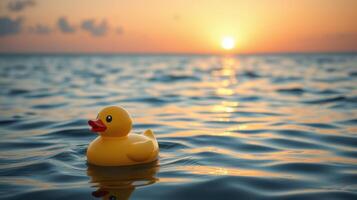 Yellow rubber duck floats on calm water as the sun sets over the horizon creating a warm evening glow photo