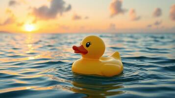 Bright yellow rubber duck floating on tranquil water during a colorful sunset near a serene beach photo