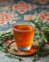 Tea served in a clear glass cup with fresh herbs on a decorative wooden coaster photo
