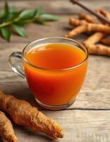 Turmeric tea served in a clear glass cup with fresh roots on a wooden table photo