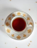 Warm cup of brewed tea on a decorative saucer surrounded by scattered tea leaves in a cozy setting photo