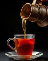 Hot tea being poured from a traditional pot into a glass cup with a saucer photo