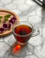 Hot tea served in a glass cup with wooden tray and purple flowers on a marble table photo